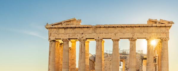 Sun hiding behind the columns of the Parthenon temple at Acropolis site on a sunny evening in...