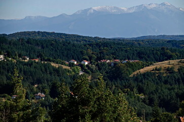 Scene with autumn meadow, forest and residential district of the Bulgarian village of Plana in the Plana mountain with the Rila mountain in the background, Bulgaria  