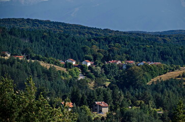 Fototapeta na wymiar Scene with autumn meadow, forest and residential district of the Bulgarian village of Plana in the Plana mountain with the Rila mountain in the background, Bulgaria 