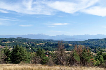 Scene with autumn meadow, forest and residential district of the Bulgarian village of Plana in the Plana mountain with the Rila mountain in the background, Bulgaria  