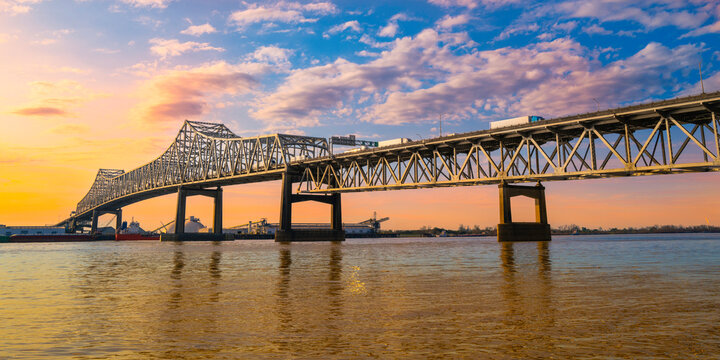 The Horace Wilkinson Bridge and Mississippi River at sunset with warm glowing clouds on the blue sky in Baton Rouge, Louisiana, USA - Powered by Adobe