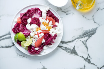Plate with radicchio, goat cheese and citrus salad, flat lay on a white marble background, horizontal shot with copyspace