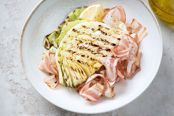 Beige plate with grilled cabbage steak and bacon, middle close-up, horizontal shot, selective focus