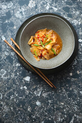Korean traditional kimchi in a dark-olive bowl, above view on a dark-brown granite background, vertical shot, copy space