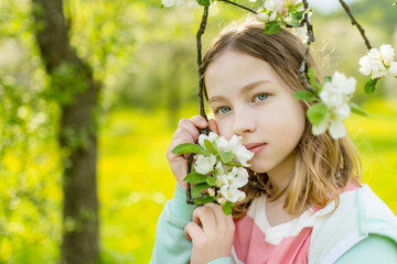 Fototapeta premium Adorable young girl in blooming apple tree garden on beautiful spring day.