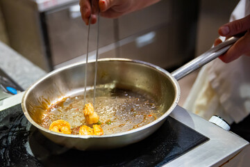man chef cooking fried shrimp in frying pan on kitchen