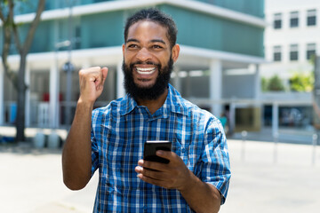 Laughing and cheering black man with phone receiving message with good news