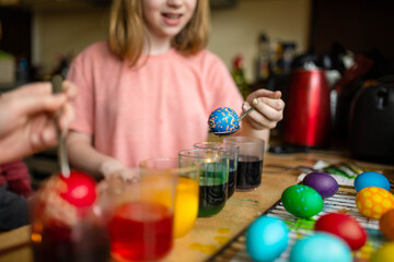 Pretty preteen girl dyeing Easter eggs at home. Child painting colorful eggs for Easter hunt. Kid getting ready for Easter celebration.