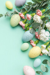 Easter colored eggs and a bouquet of white and pink carnations with eucalyptus branches on a soft green background.