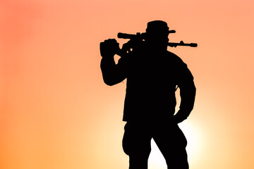 silhouette of a sniper with a rifle over his shoulder against the sunset