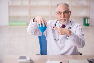 Old male doctor gastroenterologist holding enema