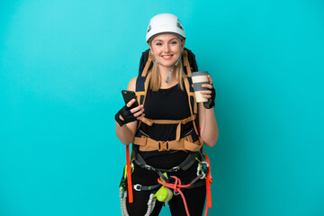 Young caucasian rock climber woman isolated on blue background holding coffee to take away and a mobile