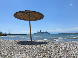 sun shades on a stony beach beside the sea with a cruise ship in the distanc