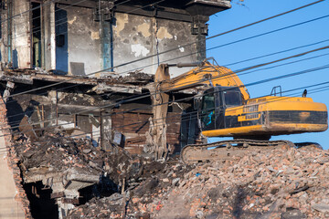 Yellow crawler excavator taking apart a building. Wires as guidlines on foreground