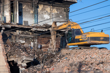 Fototapeta premium Yellow crawler excavator taking apart a building. Wires as guidlines on foreground