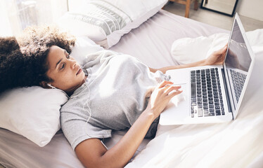 Music earphones, woman and laptop in bed in bedroom for social media or internet browsing in the morning. Technology, relax or black female with computer for streaming podcast, audio or radio in home