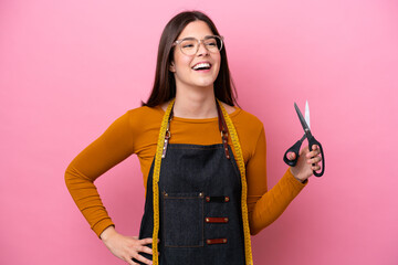 Young Brazilian seamstress woman isolated on pink background posing with arms at hip and smiling