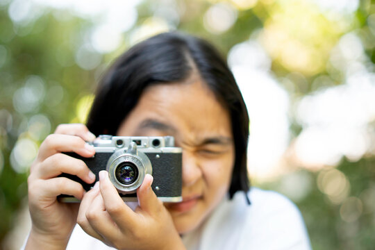 woman taking a picture with a camera, film camera in the hands of a girl taking a picture. Green trees bokeh background, woman taking a photo with a camera, selective focus, soft focus.