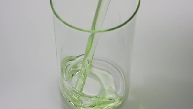 Crane shot of green tea oil is being poured into empty beaker on grey background | Abstract anti-aging cosmetics ingredients formulating concept