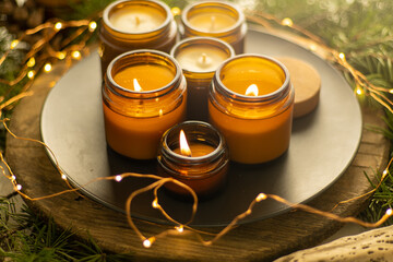 Soy candles burn in glass jars. Comfort at home. Candle in a brown jar. Scent and light. Scented handmade candle. Aroma therapy. Christmas tree and winter mood. Cozy decor. Festive garland decoration