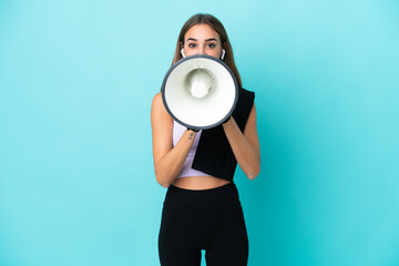 Young sport woman isolated on blue background shouting through a megaphone