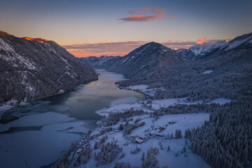 Fototapeta na wymiar The beautiful setting of the Weissensee Nature Park. Frozen Lake Weissensee, Carinthia, Alps, Austria. Aerial drone shot in January 2022. Sunset time.