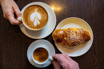 Malmo, Sweden Two coffees on a cafe table with a sweet bun and hands.