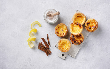 Pasteis de nata, typical Portuguese egg tart pastries on a set table with cinnamon sticks sugar powder and lemon zest. Top view with copy space