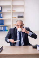 Old male employee drinking tea in the office