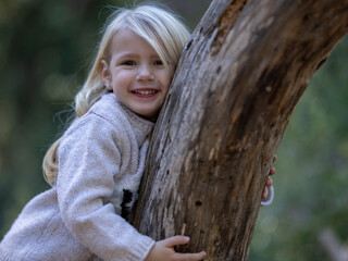 Smiling blonde little girl leaning on fallen tree