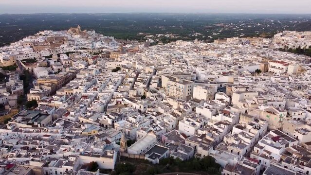 Aerial drone footage of Ostuni - La Citta Bianca (white city), Puglia, Italy at sunset. Reveal scene of medieval historic old town, landmark tourist destination and new part from above.