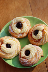Italian traditional fried Zeppole for St. Joseph (Father’s day). Homemade sweet pastry with custard cream and black cherries on a green plate on wooden table