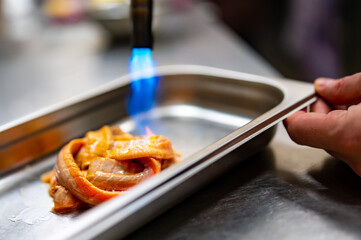 Chef fries salmon fish with a gas burner in a kitchen