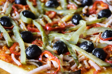 Part of freshly prepared Italian homemade pizza: olives, ham, pepper, sauce, cucumber, cheese. Close-up. Selective focus.