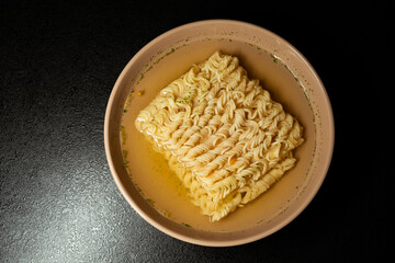 egg instant noodles are poured with water in a plate on a black background