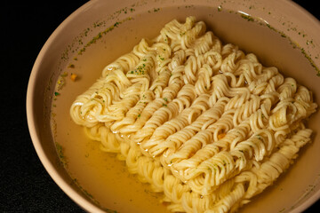 egg instant noodles are poured with water in a plate on a black background