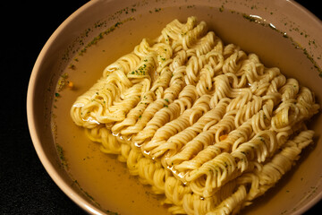 egg instant noodles are poured with water in a plate on a black background