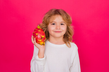 Vitamin and healthy fruits for kids. Kid hold dragon fruit in studio. Studio portrait of cute child with dragon fruit isolated on red background, copy space.