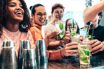 Bartender preparing cocktail mojito at pub - Happy smiling friends toasting cocktail at bar...
