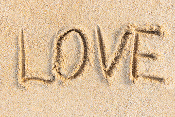 Love word written close-up on the sand surface, textured beach background
