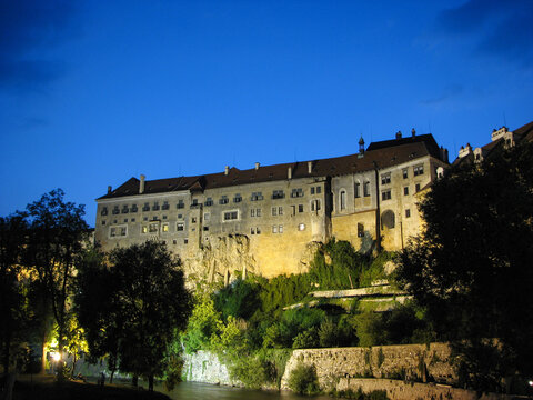 Cesky Krumlov's famous medieval castle lit up at night with a view of the Vltava River below. Image has copy space.