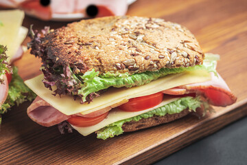 Sandwich with a ham, cheese, tomato, salad lettuce on a wooden board. Lunch concept with copy-space