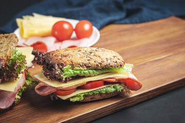 Sandwich with a ham, cheese, tomato, salad lettuce on a wooden board. Lunch concept with copy-space