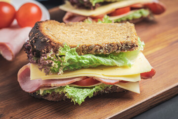 Sandwich with a ham, cheese, tomato, salad lettuce on a wooden board. Lunch concept with copy-space