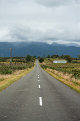 Fototapeta na wymiar Gerade asphaltierte Straße an der Westküste Neuseelands mit Bergen und Wolken.