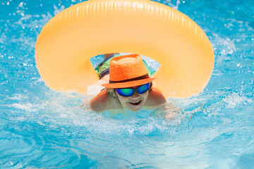 Child playing in swimming pool. Kids holidays and vacation concept. Summer kids cocktail. Happy little boy with inflatable ring in swimming pool.