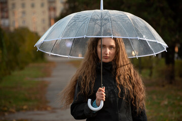 Sad young woman with umbrella in park. Seasonal portrait. Young woman with long brown heir under umbrella.