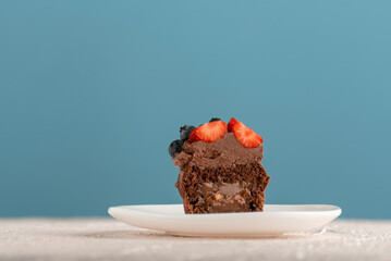 Chocolate brown cupcake decorated chocolate cream and berries on glass plate. Muffins with butter glaze. Blue background