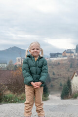 Portrait of cute fair-haired girl with two ponytails wears warm green autumn jacket on village background.Vertical frame