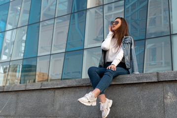 Attractive young woman in sunglesses in youth clothing on the city street. Stylish woman resting on city street.